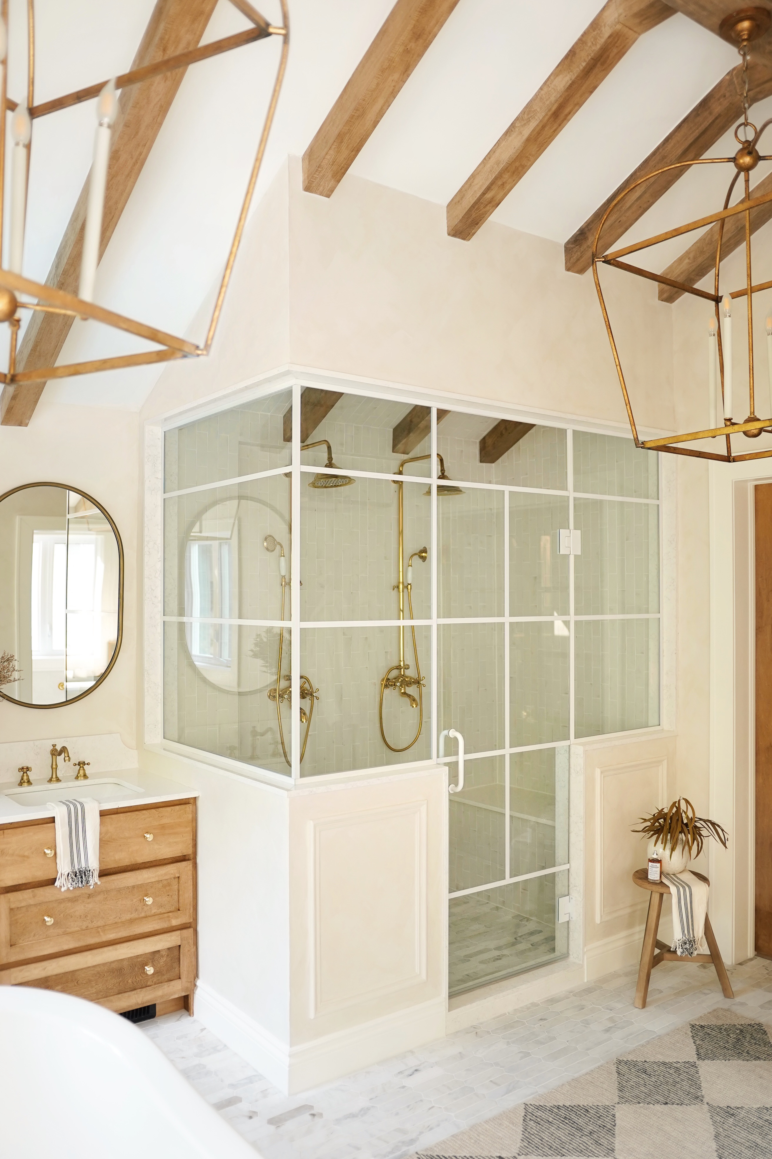 Salle de bain luxueuse avec douche vitrée, poutres en bois et robinetterie dorée